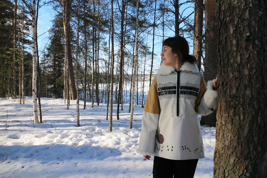 A woman wearing a jacket in snow covered woods, standing next to a tree.